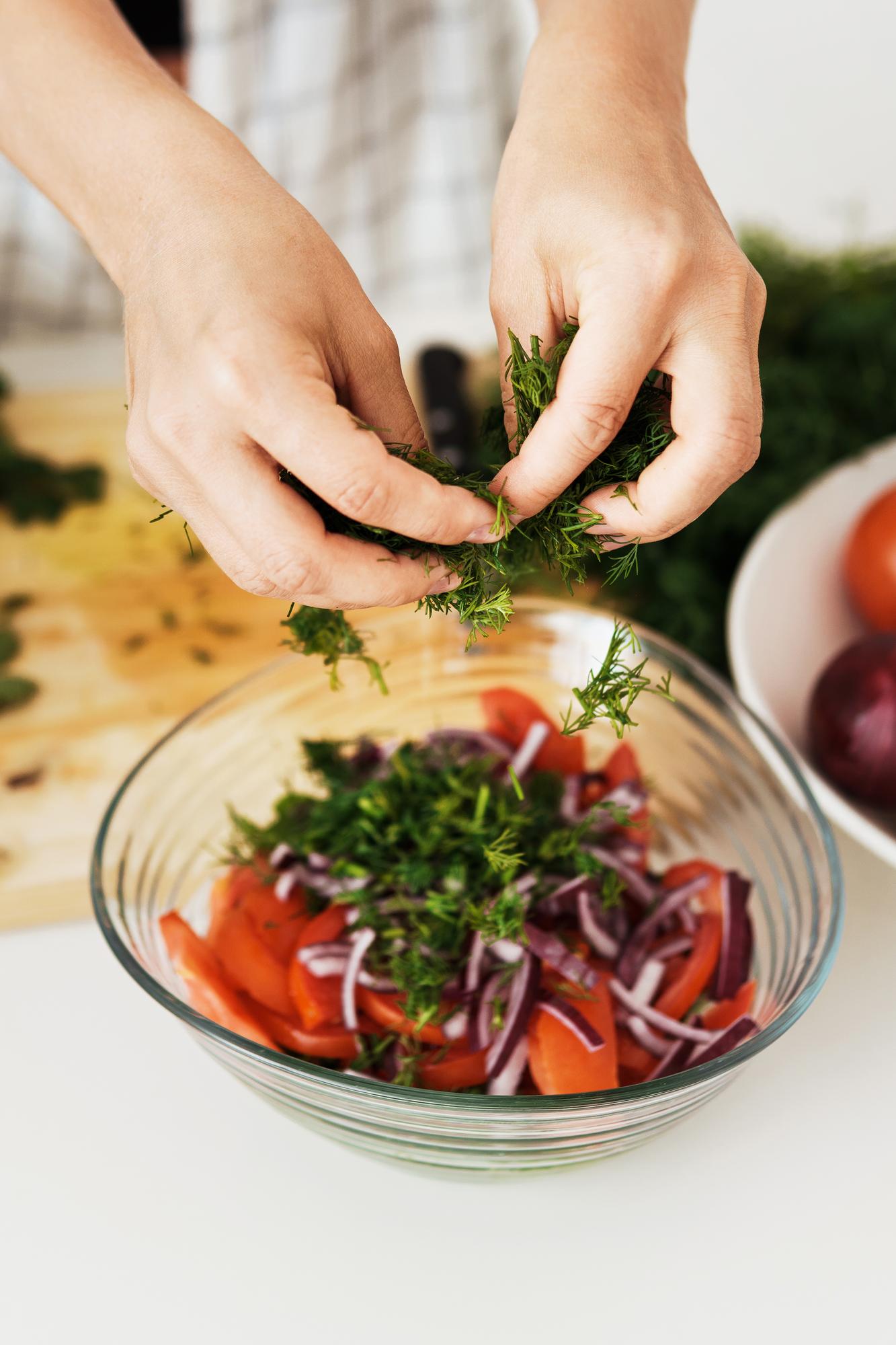 Close-up of hands preparing seasonal salad with herbs
